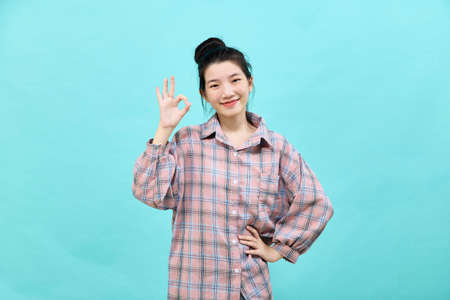 Portrait of a happy attractive young woman Asian posing in studio showing ok gestureの写真素材