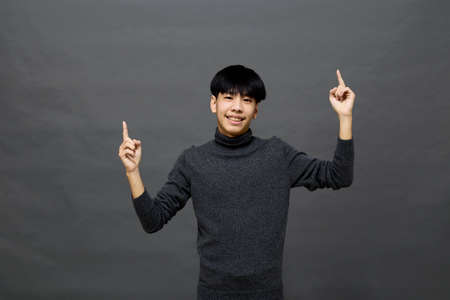 Young handsome Asian man posing to copy space on gray isolated backgroundの写真素材