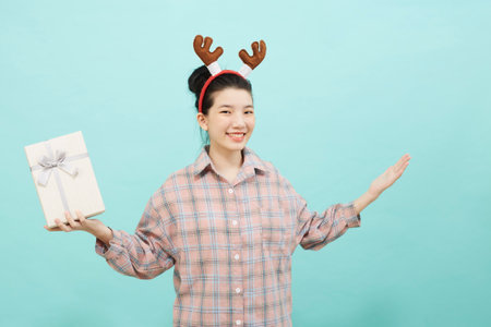 Cheerful cute Asian woman holding a gift box with a credit card on bright blue color background. Christmas and new year sales joy conceptの写真素材