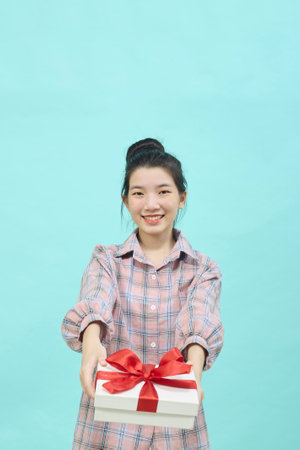 Cheerful cute Asian woman holding a gift box with a credit card on bright blue color background. Christmas and new year sales joy conceptの写真素材