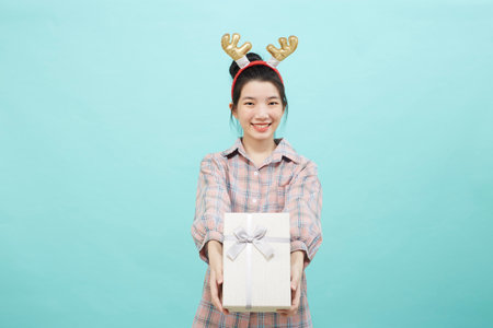 Cheerful cute Asian woman holding a gift box with a credit card on bright blue color background. Christmas and new year sales joy conceptの写真素材