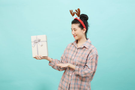 Cheerful cute Asian woman holding a gift box with a credit card on bright blue color background. Christmas and new year sales joy conceptの写真素材