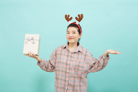 Cheerful cute Asian woman holding a gift box with a credit card on bright blue color background. Christmas and new year sales joy conceptの写真素材