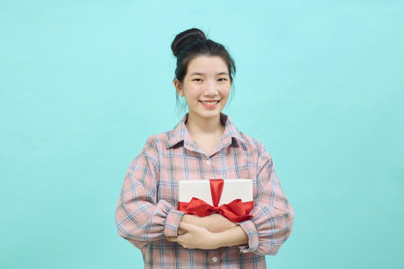 Cheerful cute Asian woman holding a gift box with a credit card on bright blue color background. Christmas and new year sales joy conceptの写真素材