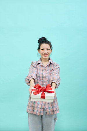 Cheerful cute Asian woman holding a gift box with a credit card on bright blue color background. Christmas and new year sales joy conceptの写真素材
