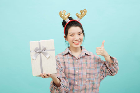 Cheerful cute Asian woman holding a gift box with a credit card on bright blue color background. Christmas and new year sales joy conceptの写真素材