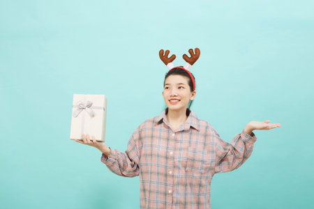 Cheerful cute Asian woman holding a gift box with a credit card on bright blue color background. Christmas and new year sales joy conceptの写真素材