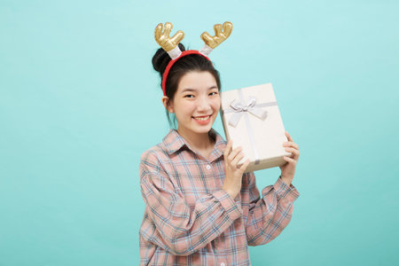 Cheerful cute Asian woman holding a gift box with a credit card on bright blue color background. Christmas and new year sales joy conceptの写真素材