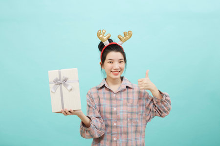 Cheerful cute Asian woman holding a gift box with a credit card on bright blue color background. Christmas and new year sales joy conceptの写真素材