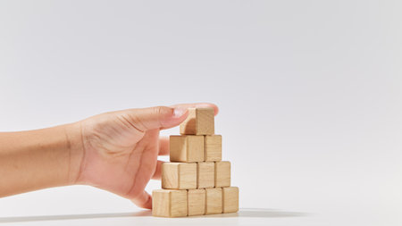 Hand putting wood cubes arrange in a pyramid shape mock-up for creating symbols or logos, business growth, and management concept on white backgroundの写真素材