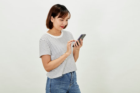 Smiling Asian woman using a smartphone, standing against texting on a mobile phone on white background, people and technology conceptの写真素材