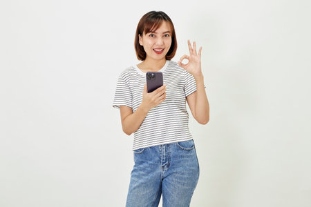 Young Asia woman holding showing mobile phone and pointing a finger empty copy space, showing promo text, standing with a smartphone against on white backgroundの写真素材