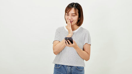 Young Asia woman holding showing mobile phone and pointing a finger empty copy space, showing promo text, standing with a smartphone against on white backgroundの写真素材