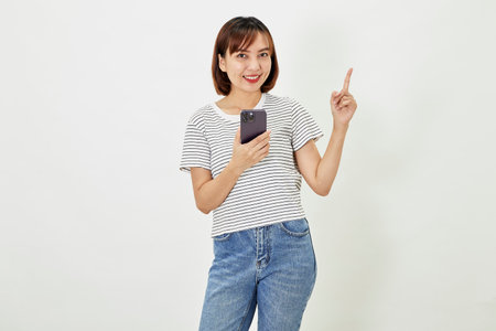 Young Asia woman holding showing mobile phone and pointing a finger empty copy space, showing promo text, standing with a smartphone against on white backgroundの写真素材