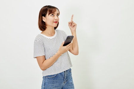 Young Asia woman holding showing mobile phone and pointing a finger empty copy space, showing promo text, standing with a smartphone against on white backgroundの写真素材