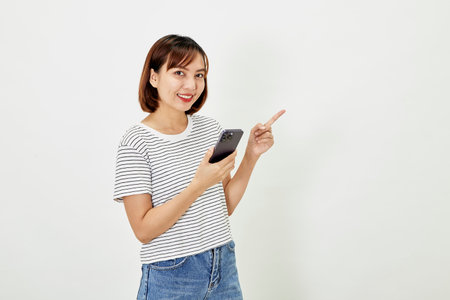 Young Asia woman holding showing mobile phone and pointing a finger empty copy space, showing promo text, standing with a smartphone against on white backgroundの写真素材