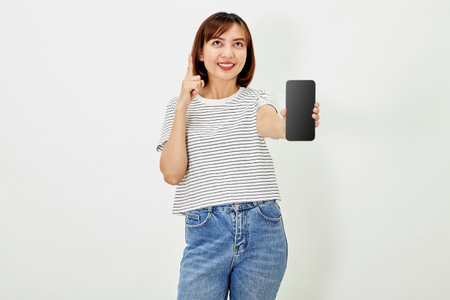 Cute asian short brunette hair woman promotes smartphone app, woman blogger showing personal social media page hold phone look camera happily smiling on white backgroundの写真素材