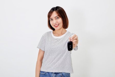 Beautiful young business Asian woman with brunette short hair wearing a t-shirt and jeans with a car key on white isolated backgroundの写真素材