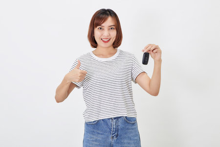 Beautiful young business Asian woman with brunette short hair wearing a t-shirt and jeans with a car key on white isolated backgroundの写真素材