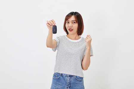 Beautiful young business Asian woman with brunette short hair wearing a t-shirt and jeans with a car key on white isolated backgroundの写真素材