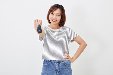 Beautiful young business Asian woman with brunette short hair wearing a t-shirt and jeans with a car key on white isolated backgroundの写真素材