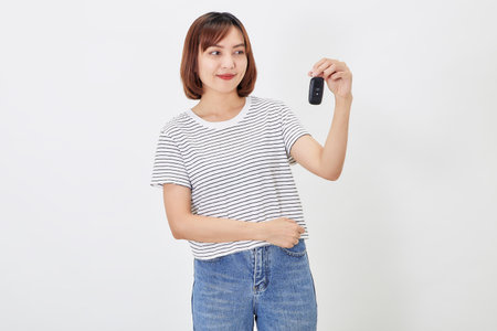 Beautiful young business Asian woman with brunette short hair wearing a t-shirt and jeans with a car key on white isolated backgroundの写真素材