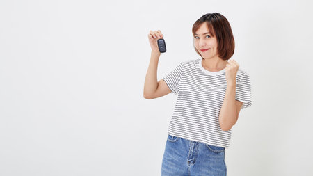 Beautiful young business Asian woman with brunette short hair wearing a t-shirt and jeans with a car key on white isolated backgroundの写真素材