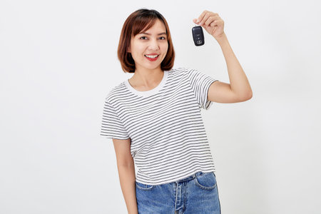 Beautiful young business Asian woman with brunette short hair wearing a t-shirt and jeans with a car key on white isolated backgroundの写真素材