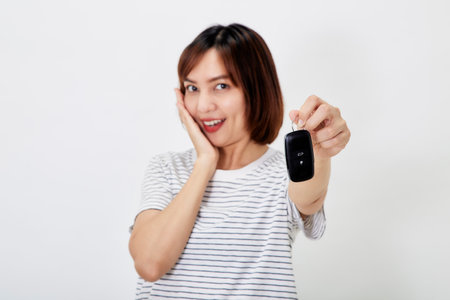 Beautiful young business Asian woman with brunette short hair wearing a t-shirt and jeans with a car key on white isolated backgroundの写真素材