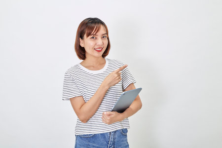 Portrait of a smiling beautiful Asian woman freelancer using a digital tablet and looking pleased with the device screen, shopping online, on white backgroundの写真素材