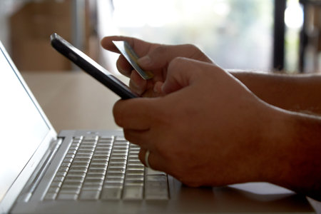 Hands holding a credit card using laptop computer and mobile phone for online shoppingの写真素材