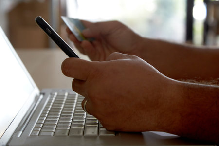 Hands holding a credit card using laptop computer and mobile phone for online shoppingの写真素材