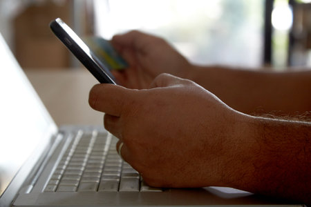 Hands holding a credit card using laptop computer and mobile phone for online shoppingの写真素材