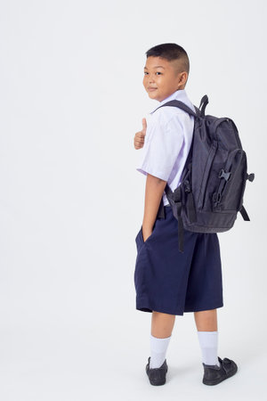 A young Asian cute boy standing in a Thai school uniform with a backpack bag and book on a white background banner. Back to schoolの写真素材