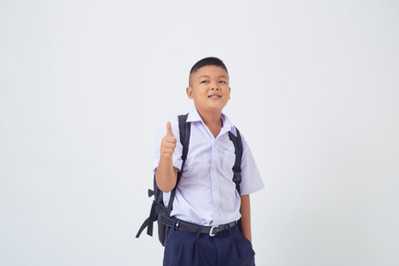 A young Asian cute boy standing in a Thai school uniform with a backpack bag and book on a white background banner. Back to schoolの写真素材