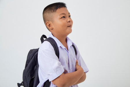 A young Asian cute boy standing in a Thai school uniform with a backpack bag and book on a white background banner. Back to schoolの写真素材