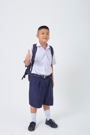 A young Asian cute boy standing in a Thai school uniform with a backpack bag and book on a white background banner. Back to schoolの写真素材