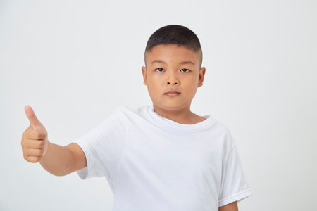 Cute smiling Asian boy in a plain white t-shirt looking at the camera in an isolated studio light white color backgroundの写真素材