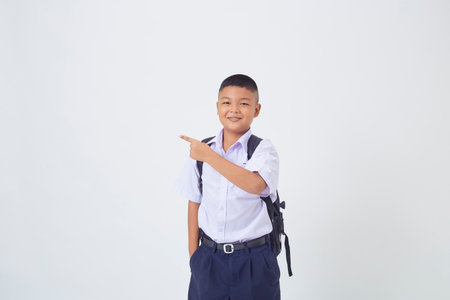 A young Asian cute boy standing in a Thai school uniform with a backpack bag and book on a white background banner. Back to schoolの写真素材