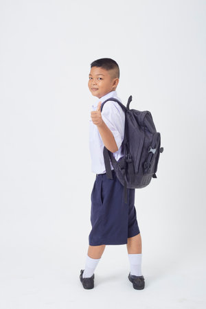 A young Asian cute boy standing in a Thai school uniform with a backpack bag and book on a white background banner. Back to schoolの写真素材