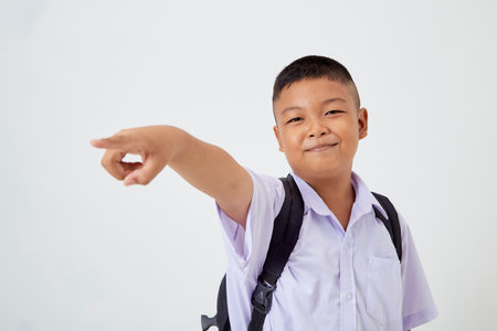 A young Asian cute boy standing in a Thai school uniform with a backpack bag and book on a white background banner. Back to schoolの写真素材
