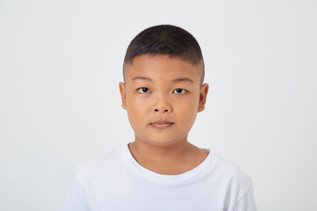 Cute smiling Asian boy in a plain white t-shirt looking at the camera in an isolated studio light white color backgroundの写真素材