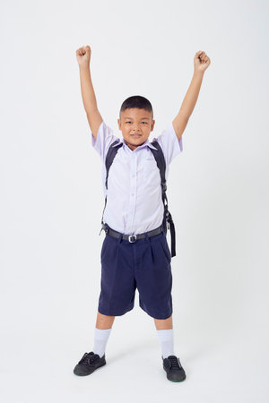 A young Asian cute boy standing in a Thai school uniform with a backpack bag and book on a white background banner. Back to schoolの写真素材
