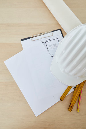 Construction tools and a white hard hat with a measuring stick, paper house building plan on a wooden work table copy space for textの写真素材