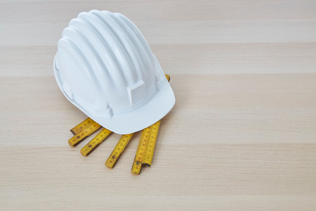 Construction tools and a white hard hat with a measuring stick, paper house building plan on a wooden work table copy space for textの写真素材