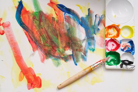 A brush put on the color palette. A child paint with colorful watercolor on the white painting paper.の写真素材