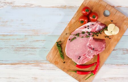 A pieces of fresh raw pork steak with tomatoes, thyme, pepper, red chili and galic on light wooden and on top with black pepper. Raw pork is ready to cook. Food and kitchen conceptの写真素材