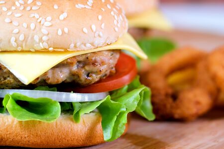 Close-up macro of delicious fresh homemade hamburger with cheese, pork, tomato, onion and vegetable on a wooden plate with french fries and onion ring.の写真素材