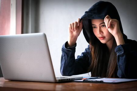 Professional hacker young women wearing blue suit with hood using laptop to steal data from other computer online system at the old building. Malware and hacker conceptの写真素材