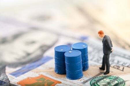 Miniature people : Business man standing in front of drums (oil). Oil trend down. The background is US dollar. Price oil down. Barrel arrow down. Business and finance concept.の写真素材